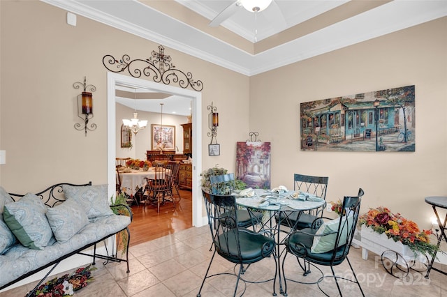 tiled dining space featuring a tray ceiling, crown molding, and ceiling fan with notable chandelier