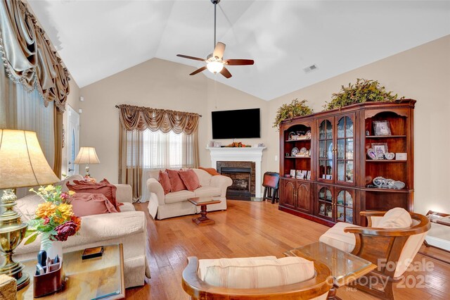 living room featuring a ceiling fan, visible vents, a fireplace with flush hearth, vaulted ceiling, and light wood-style floors