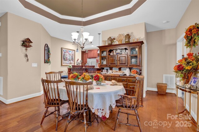 dining area with light wood finished floors, visible vents, a chandelier, and a raised ceiling