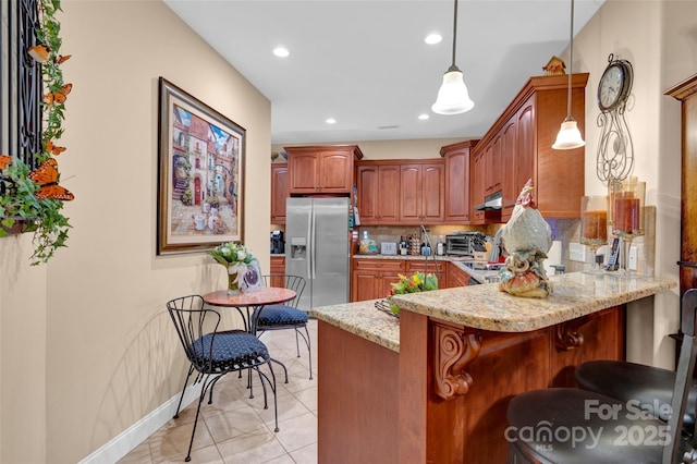 kitchen featuring light stone counters, under cabinet range hood, tasteful backsplash, a peninsula, and stainless steel fridge with ice dispenser