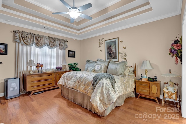 bedroom with light wood finished floors, visible vents, ceiling fan, ornamental molding, and a raised ceiling