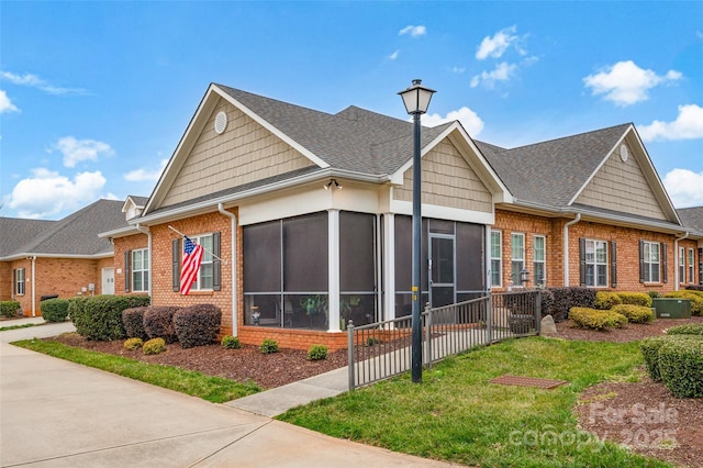 view of front facade featuring brick siding, a shingled roof, a front yard, and a sunroom