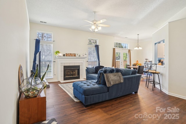 living area featuring a tiled fireplace, visible vents, a healthy amount of sunlight, and dark wood-style flooring