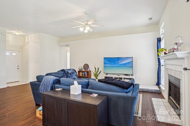 living room with visible vents, a fireplace, a ceiling fan, and dark wood-style flooring