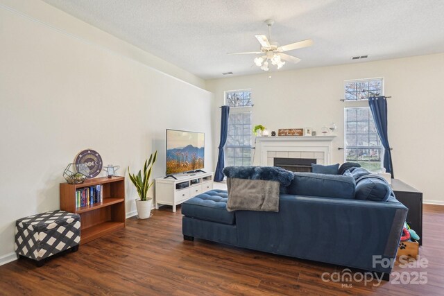 living room featuring a ceiling fan, wood finished floors, visible vents, a tile fireplace, and a textured ceiling