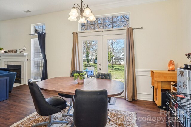 dining area with visible vents, a fireplace, french doors, an inviting chandelier, and dark wood-style flooring