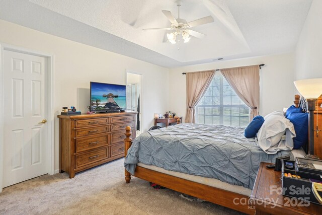 carpeted bedroom featuring a tray ceiling, visible vents, and ceiling fan