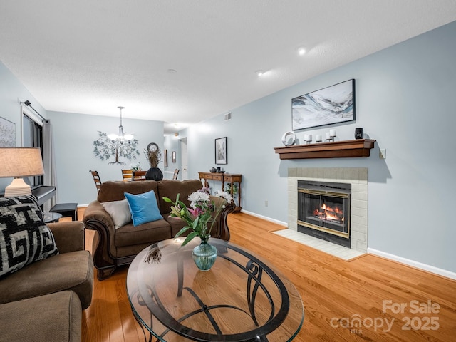 living room with a brick fireplace, baseboards, an inviting chandelier, and wood finished floors