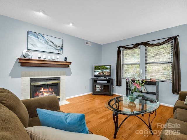 living area with visible vents, a tile fireplace, baseboards, and wood finished floors