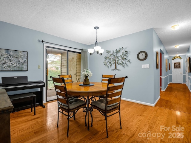 dining space with light wood finished floors, baseboards, a textured ceiling, and an inviting chandelier