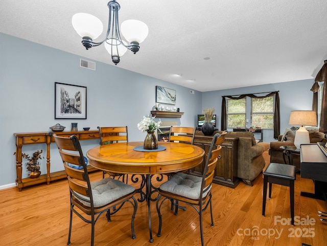 dining room with a textured ceiling, light wood-style flooring, visible vents, and a chandelier