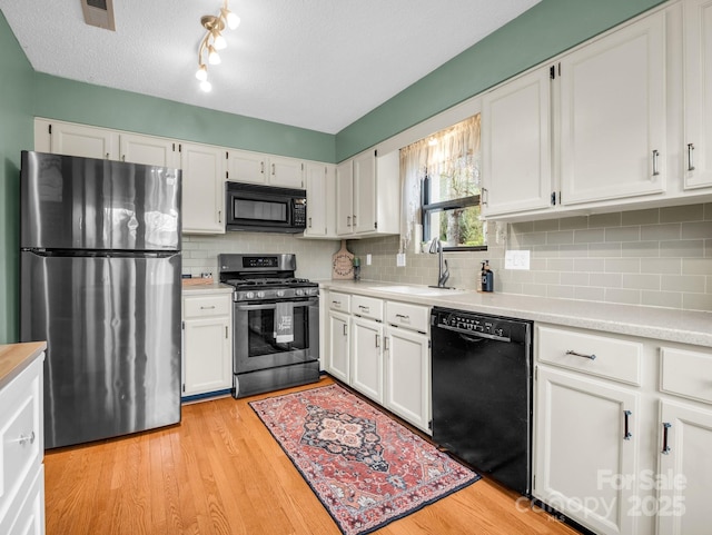 kitchen featuring visible vents, a sink, black appliances, white cabinetry, and light wood-type flooring