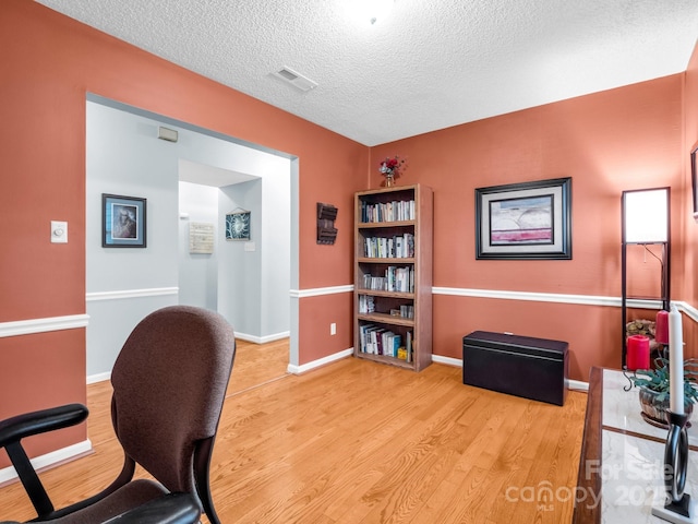 home office with baseboards, wood finished floors, visible vents, and a textured ceiling