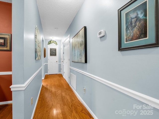 corridor featuring visible vents, a textured ceiling, baseboards, and wood finished floors