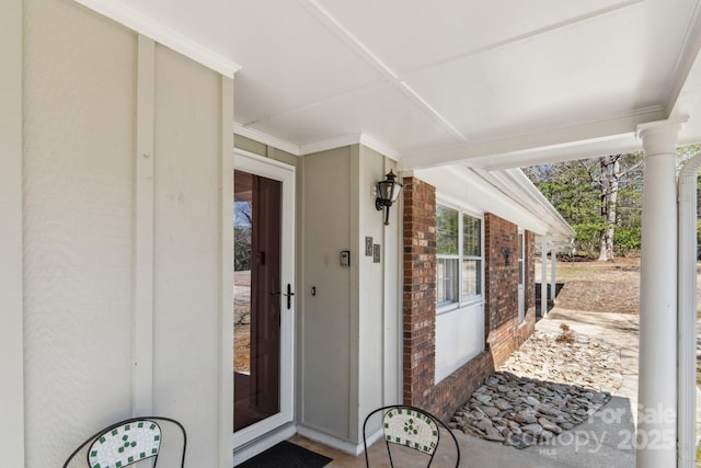 doorway to property featuring a porch and brick siding