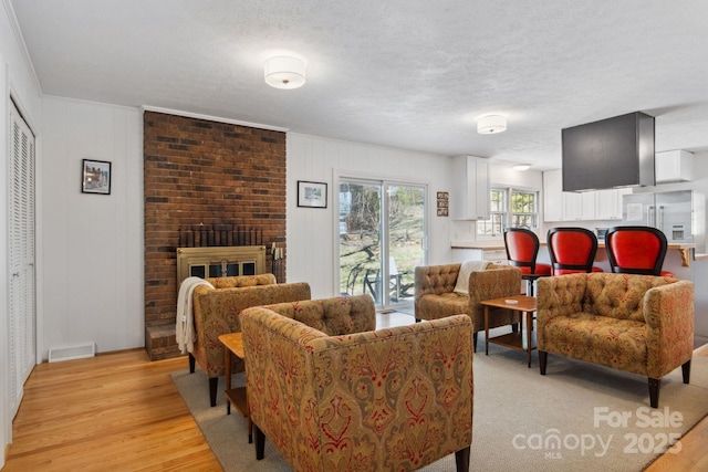 living room featuring a textured ceiling, light wood finished floors, a fireplace, and visible vents