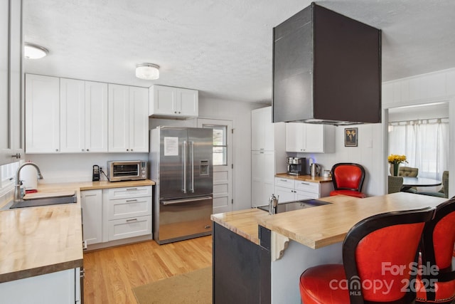 kitchen featuring high end fridge, butcher block counters, a sink, and a breakfast bar area