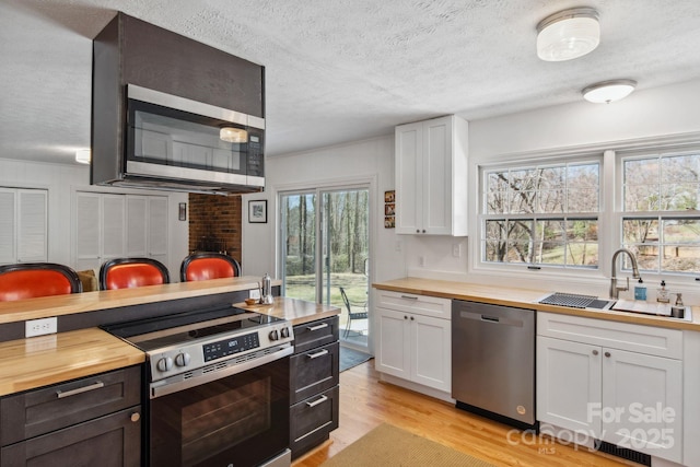 kitchen with butcher block counters, appliances with stainless steel finishes, white cabinets, and a sink