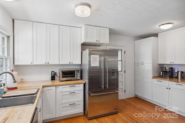 kitchen featuring a toaster, butcher block countertops, a sink, white cabinetry, and appliances with stainless steel finishes