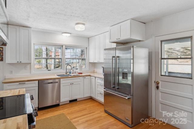 kitchen featuring stainless steel appliances, light wood-style flooring, white cabinetry, a sink, and butcher block countertops