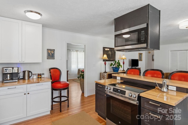 kitchen featuring electric range, butcher block counters, and white cabinetry