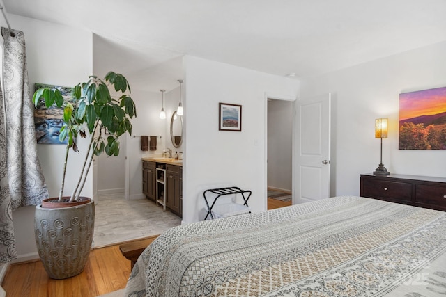 bedroom with light wood-style floors, baseboards, a sink, and ensuite bath