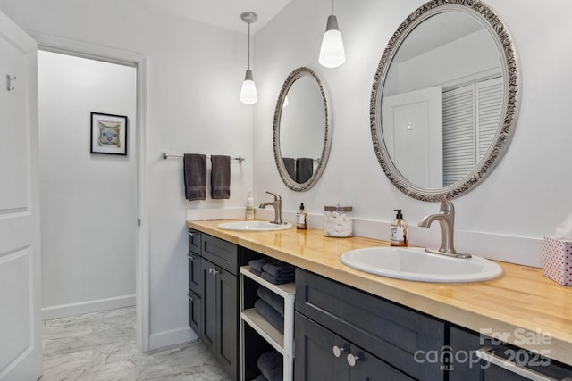 bathroom with marble finish floor, double vanity, a sink, and baseboards