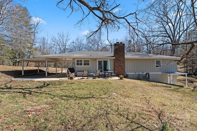 rear view of house with an attached carport, a patio area, a yard, and a chimney