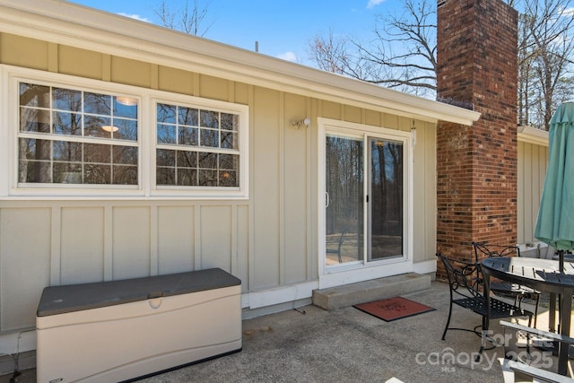 view of exterior entry with board and batten siding, outdoor dining area, a patio, and a chimney