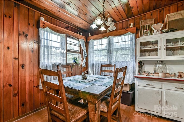 dining area featuring an inviting chandelier, wooden walls, light wood-style floors, and a healthy amount of sunlight