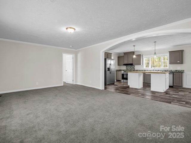 unfurnished living room with arched walkways, a textured ceiling, crown molding, dark carpet, and a sink