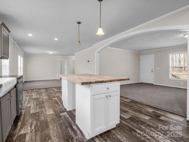 kitchen featuring open floor plan, ornamental molding, a kitchen island, and wood counters