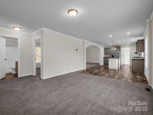 unfurnished living room featuring arched walkways, crown molding, visible vents, dark carpet, and a sink