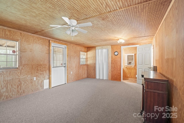 carpeted empty room featuring wooden walls, wood ceiling, and ceiling fan