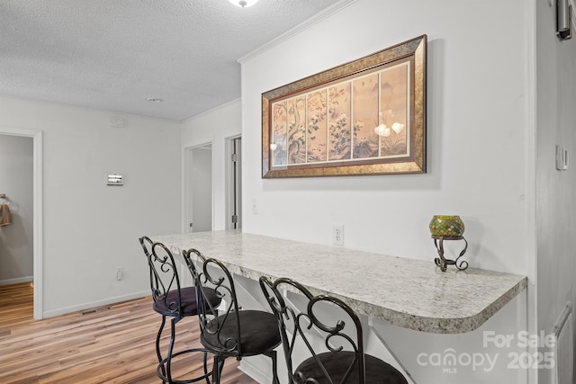 kitchen featuring a kitchen bar, light wood finished floors, a textured ceiling, light countertops, and baseboards