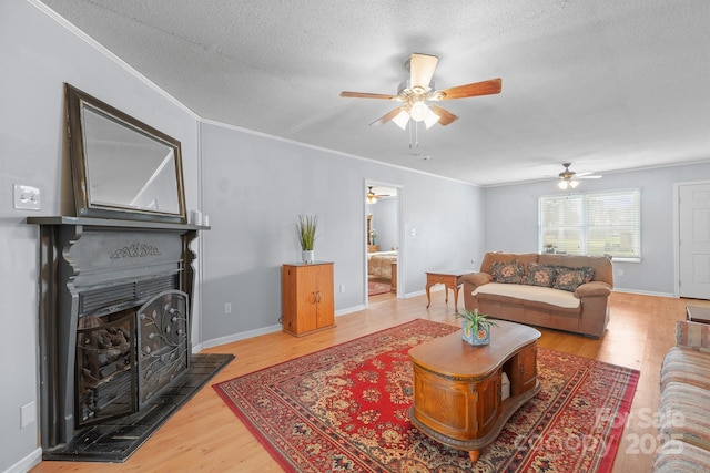 living area with a textured ceiling, wood finished floors, a fireplace, crown molding, and baseboards