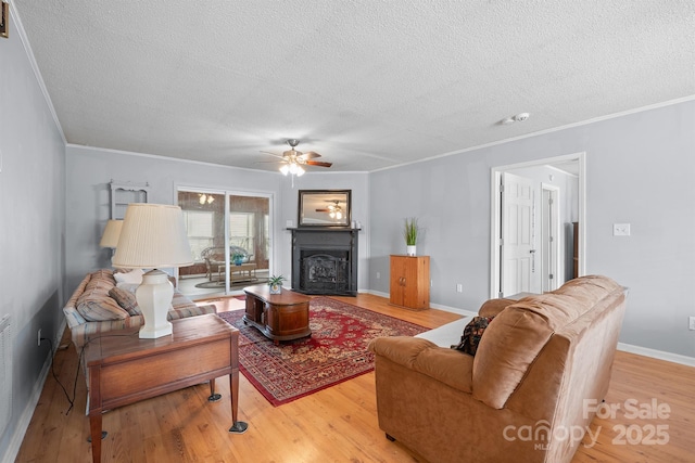 living area featuring baseboards, light wood finished floors, a fireplace, ornamental molding, and a textured ceiling