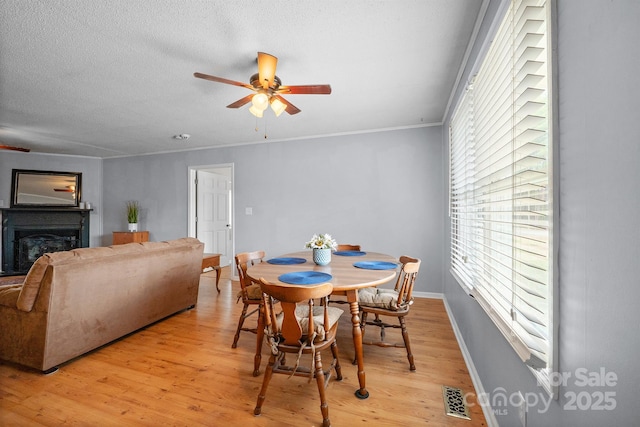 dining space featuring light wood-style flooring, a fireplace, visible vents, and ceiling fan