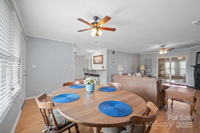 dining area featuring a ceiling fan, baseboards, ornamental molding, a textured ceiling, and light wood-type flooring