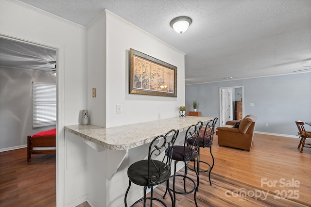 kitchen with a breakfast bar area, wood finished floors, light countertops, and ornamental molding