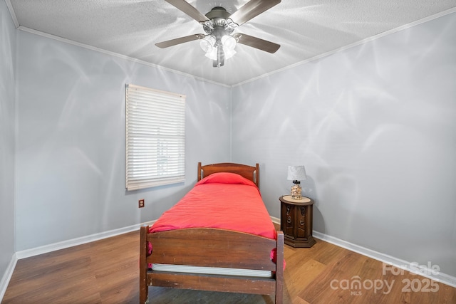 bedroom with ornamental molding, a textured ceiling, wood finished floors, baseboards, and ceiling fan