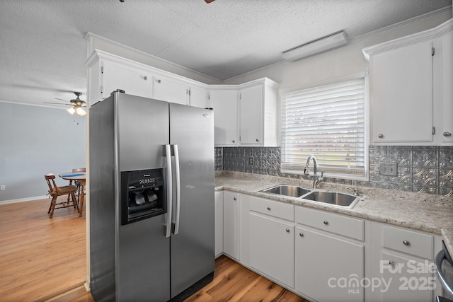 kitchen with light wood-type flooring, stainless steel refrigerator with ice dispenser, a sink, tasteful backsplash, and light countertops