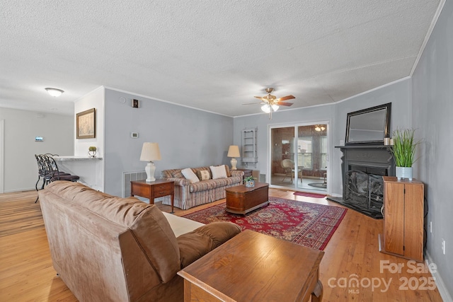 living room featuring a fireplace with raised hearth, a textured ceiling, crown molding, and light wood-style floors