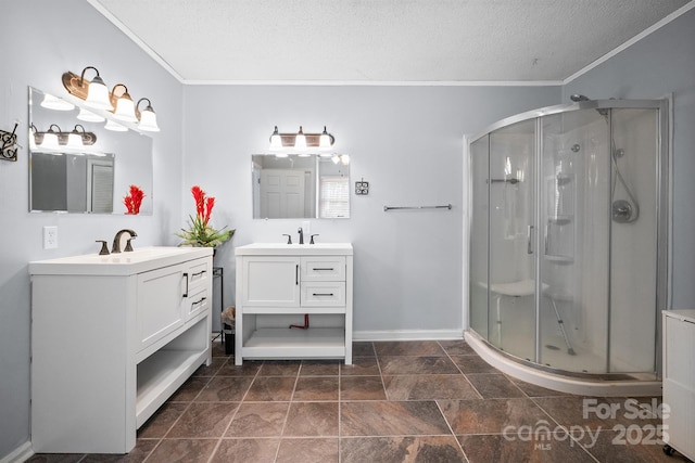 full bath with two vanities, a sink, a shower stall, a textured ceiling, and crown molding