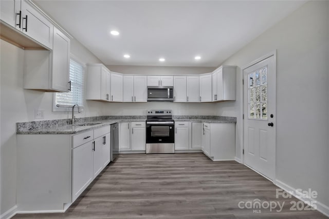 kitchen featuring wood finished floors, stainless steel appliances, white cabinetry, a sink, and recessed lighting