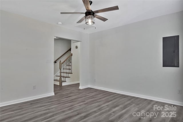 spare room featuring a ceiling fan, baseboards, stairs, electric panel, and dark wood finished floors