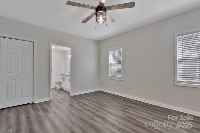 unfurnished bedroom featuring a closet, dark wood-style flooring, connected bathroom, and baseboards