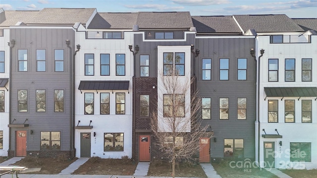 townhome / multi-family property featuring board and batten siding, a standing seam roof, brick siding, and metal roof