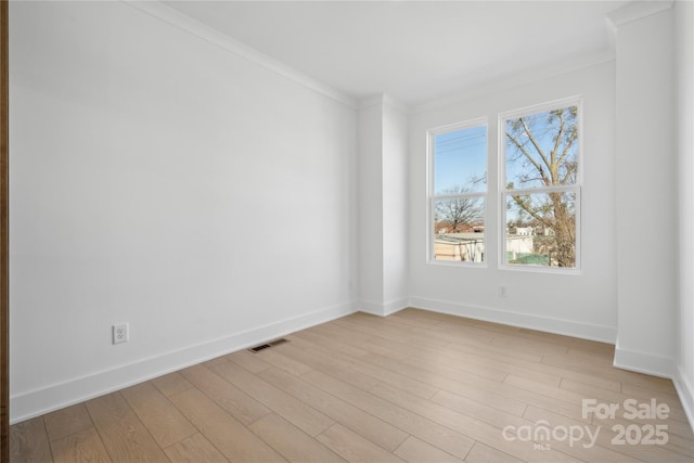 empty room featuring baseboards, light wood finished floors, visible vents, and crown molding