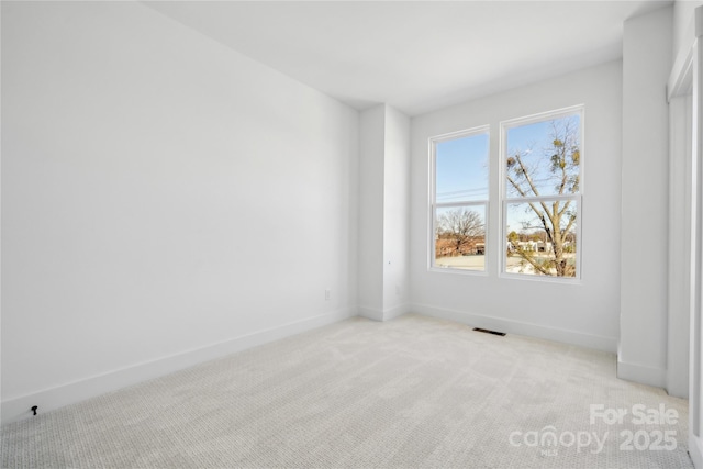 spare room featuring light colored carpet, visible vents, and baseboards